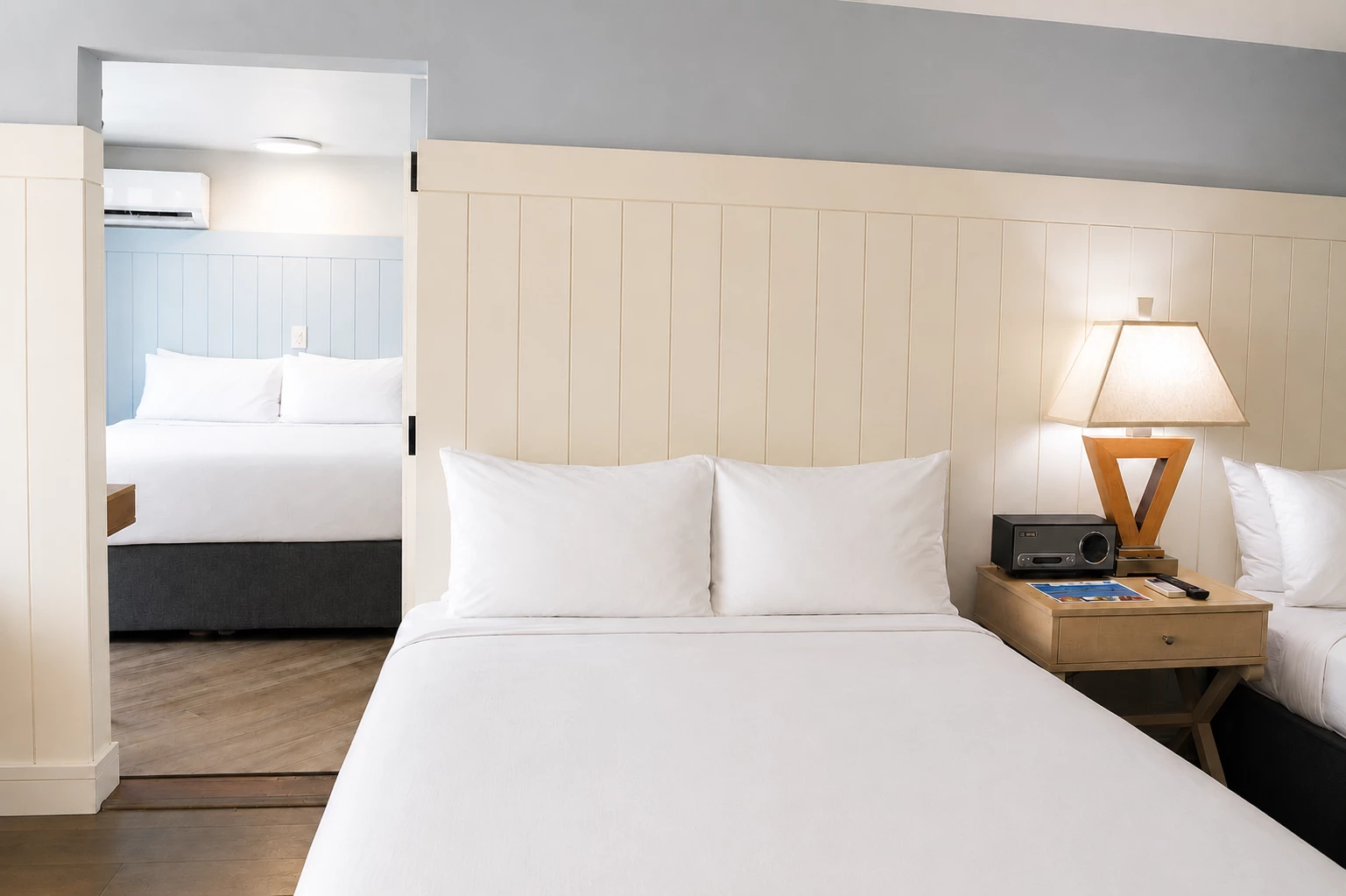 A hotel room with two beds, a wooden nightstand, and a lamp.
