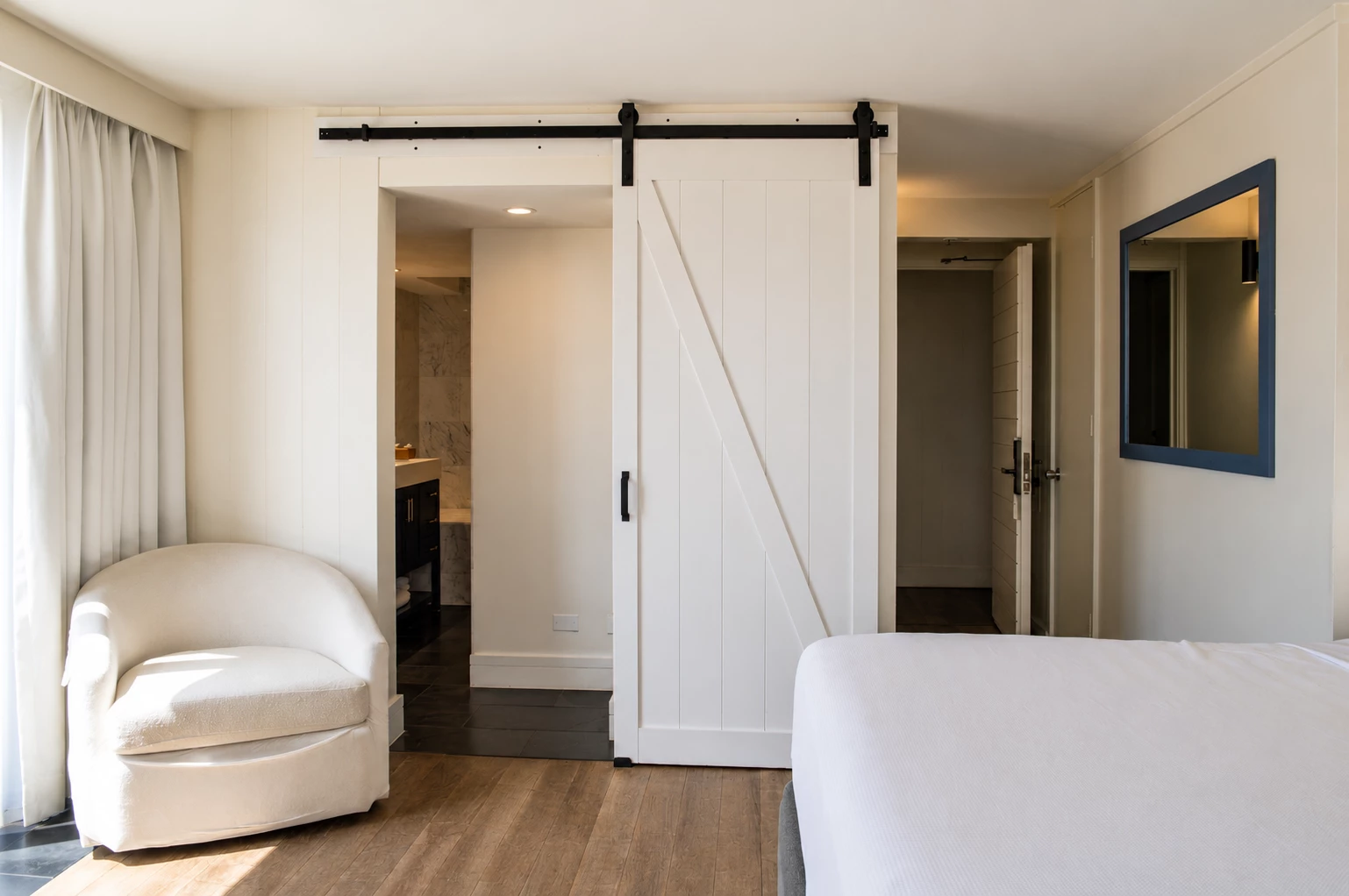 A hotel room with a white bed, chair, and sliding barn door.