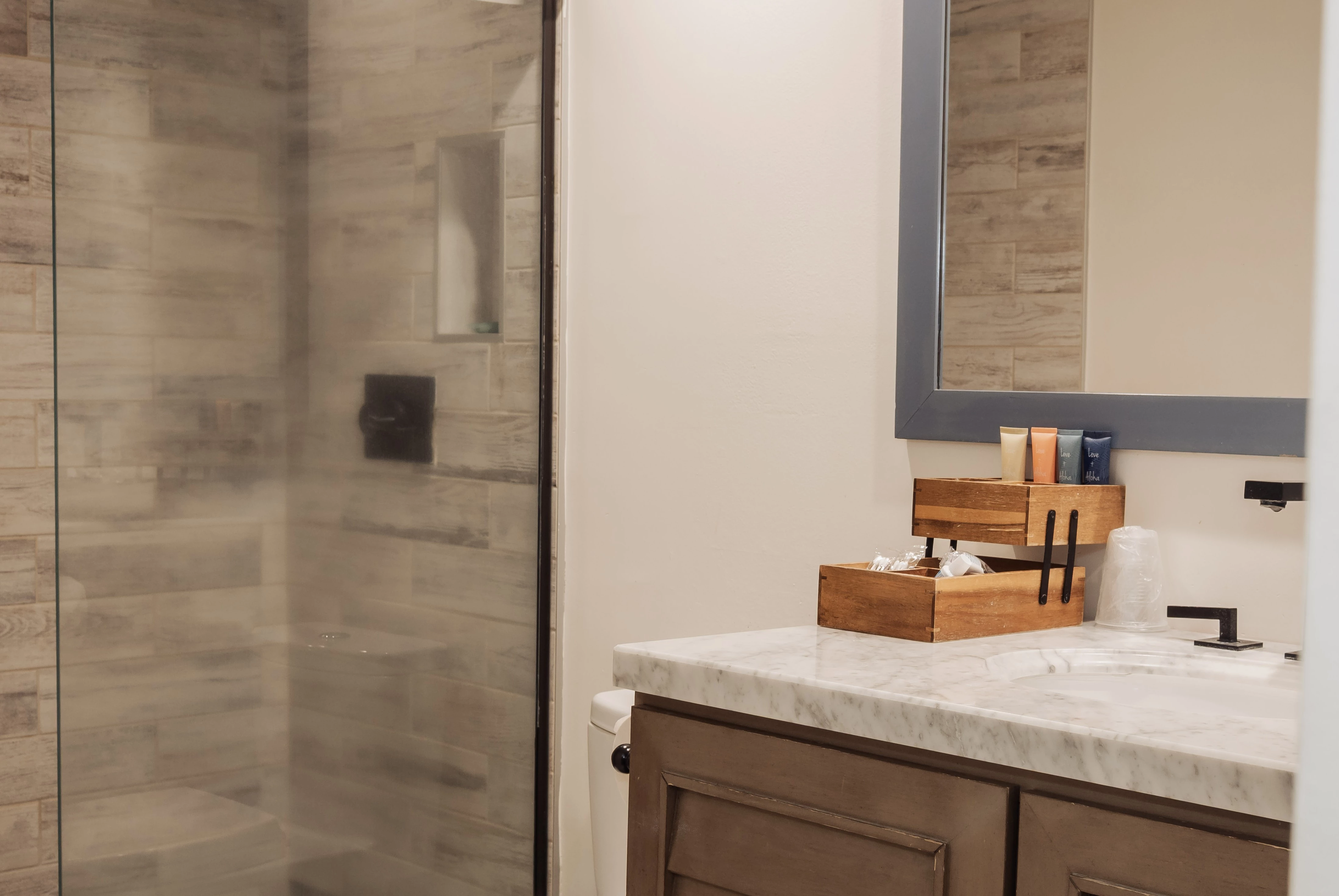 A bathroom with a marble countertop, wooden cabinets, and a glass shower door.
