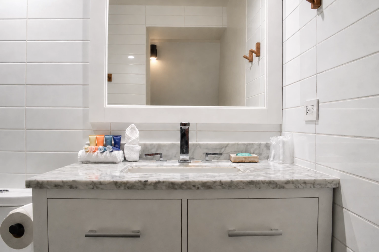 A clean and modern bathroom with a marble countertop, gray cabinets, and white tile walls.