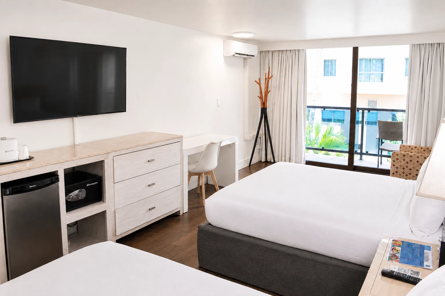 A hotel room with two double beds, a desk, a TV, a minibar, and a balcony with a view.