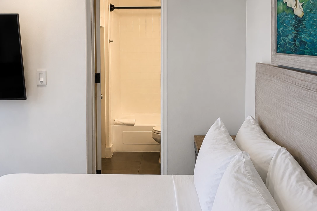 A hotel room with a bed, pillows, and a bathroom doorway.