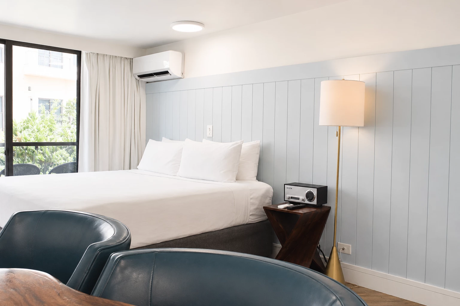 A hotel room with a bed, two chairs, a lamp, and a radio.
