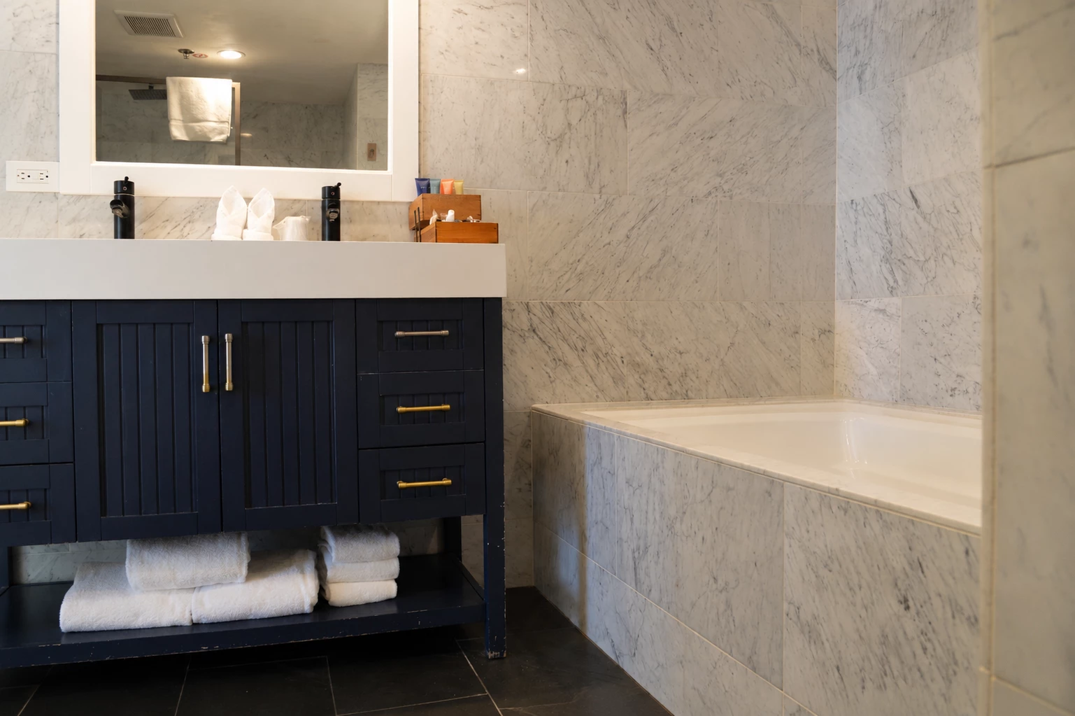 A bathroom vanity with a large mirror and a bathtub in the background.
