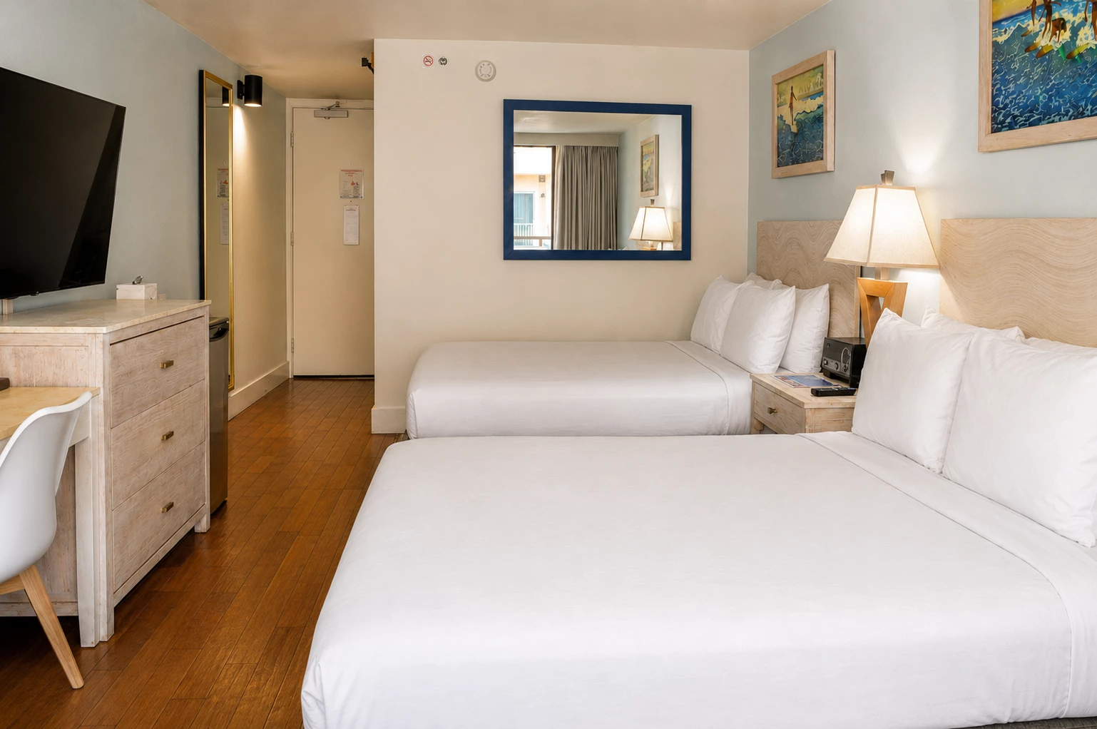 A hotel room with two beds, a desk, TV, and mirror.