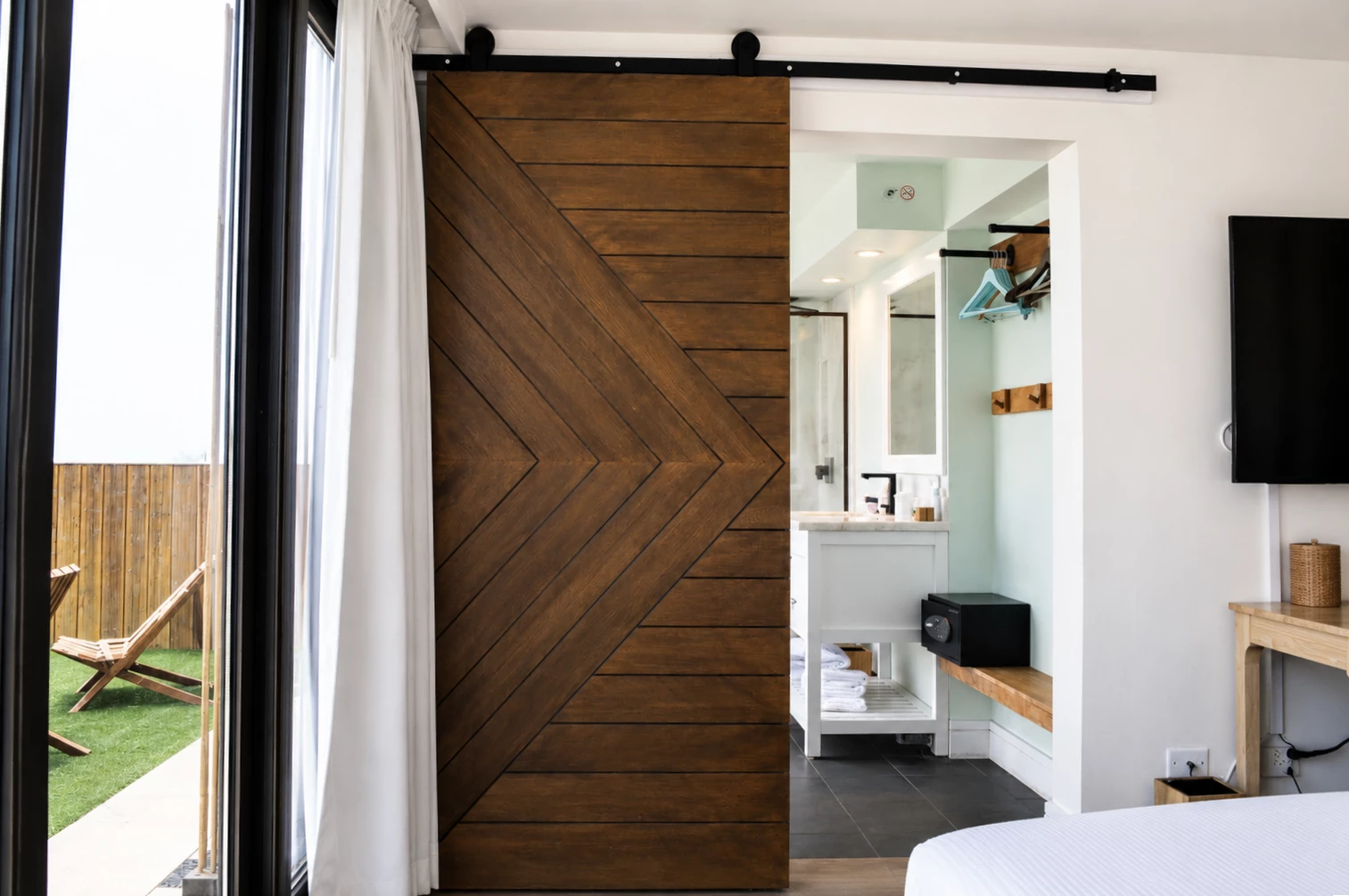 A room with a sliding barn door, a bed, and a bathroom in the background.