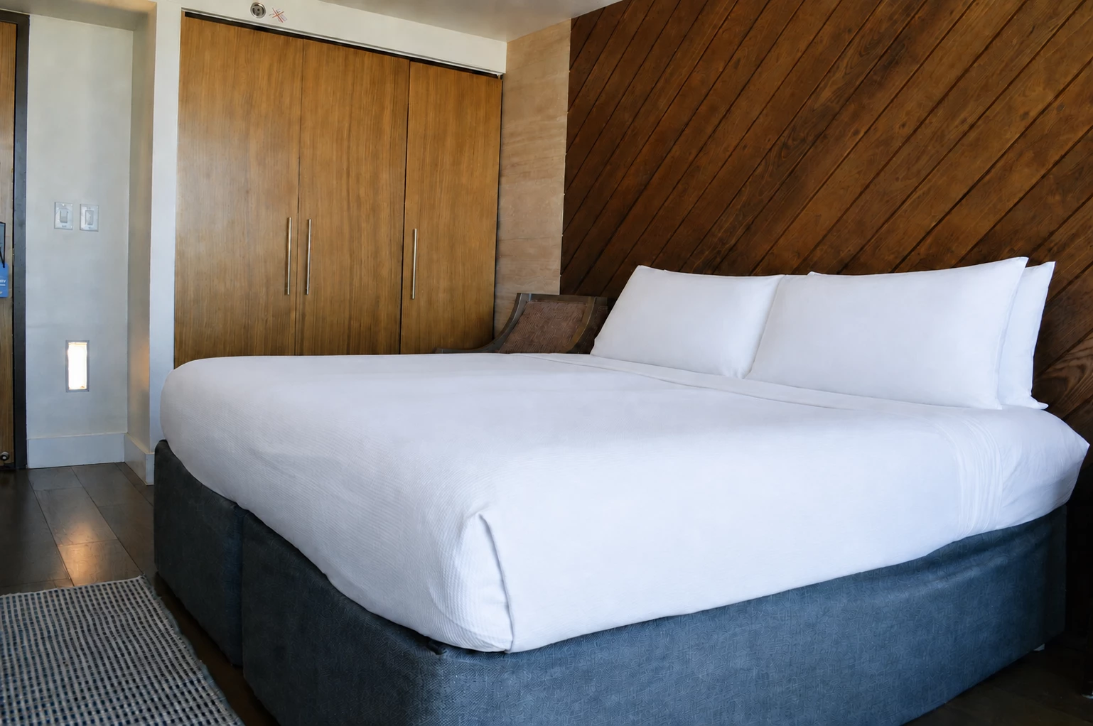 A neatly made bed with white bedding and two pillows in a room with wood paneling and a closet.