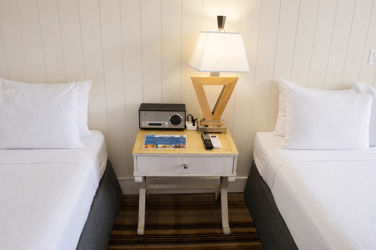 A hotel room with two beds and a nightstand between them.
