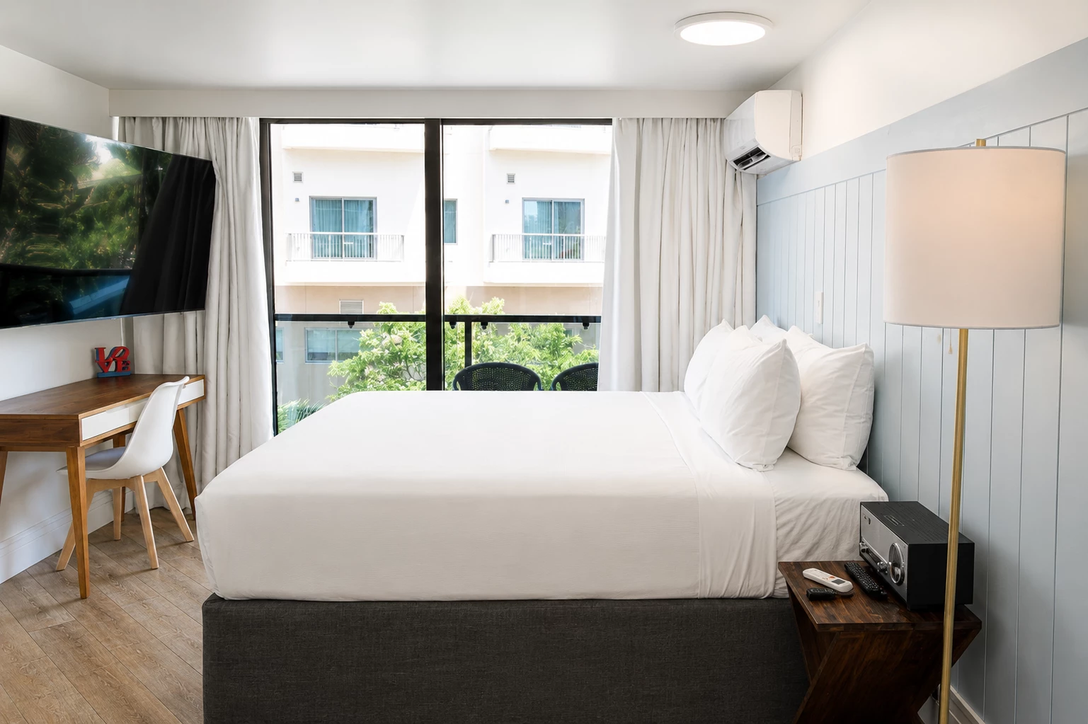 A clean and modern hotel room with a large bed, desk, TV, and window with a view.
