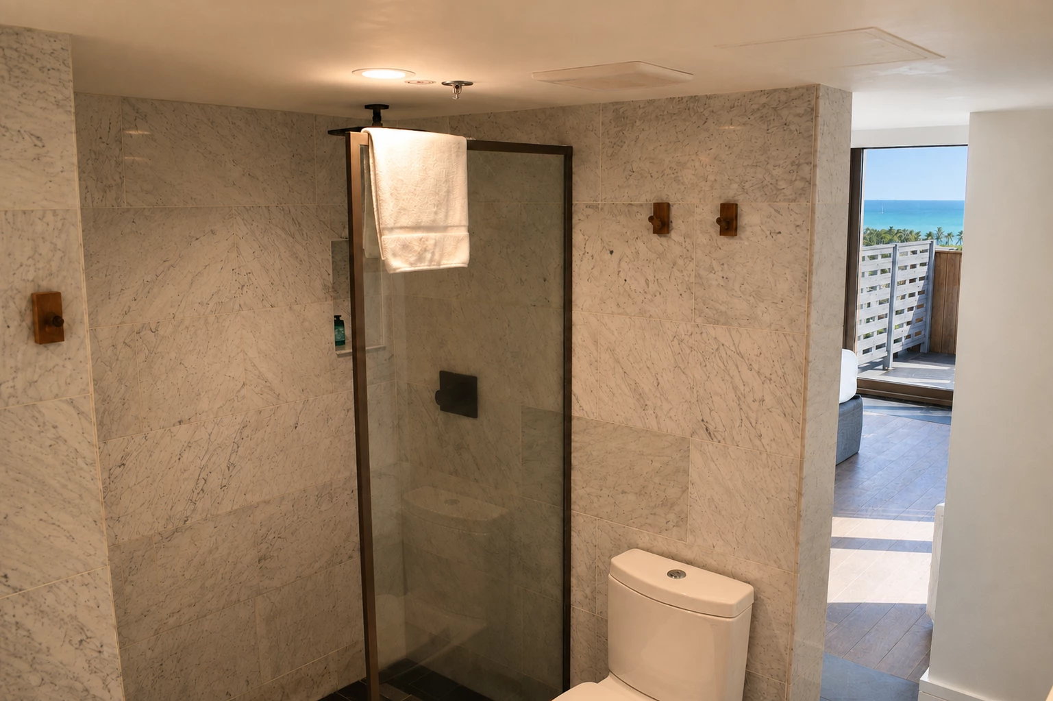A bathroom with a marble shower, toilet, and ocean view.