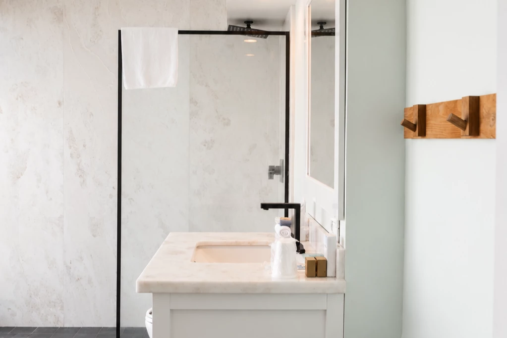A modern bathroom with a marble countertop, glass shower door, and black faucet.