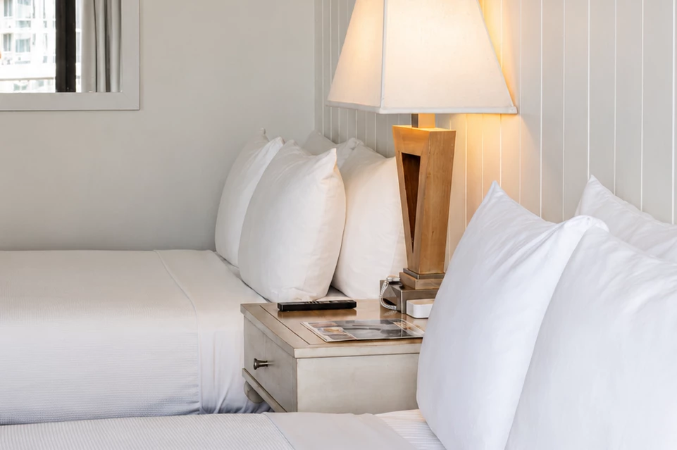 A close-up of a bed with white pillows and bedding, a lamp, and a nightstand.