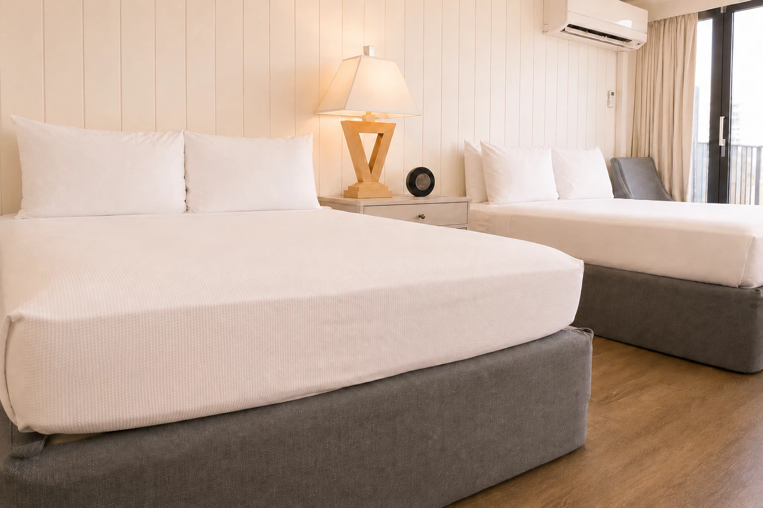 A hotel room with two double beds, a wooden floor, and a panelled wall.
