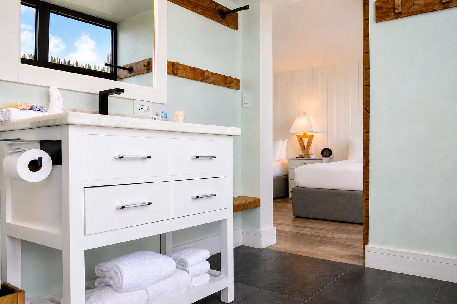 A bathroom with a white vanity and a view of a bed in the background