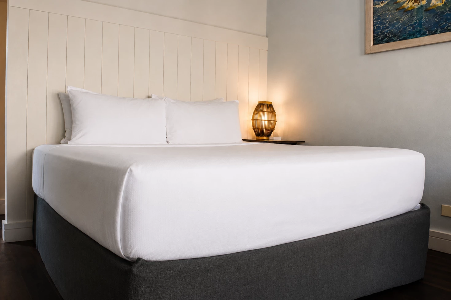 A neatly made bed with white bedding and a gray bed frame, with a table lamp on a small table beside it.