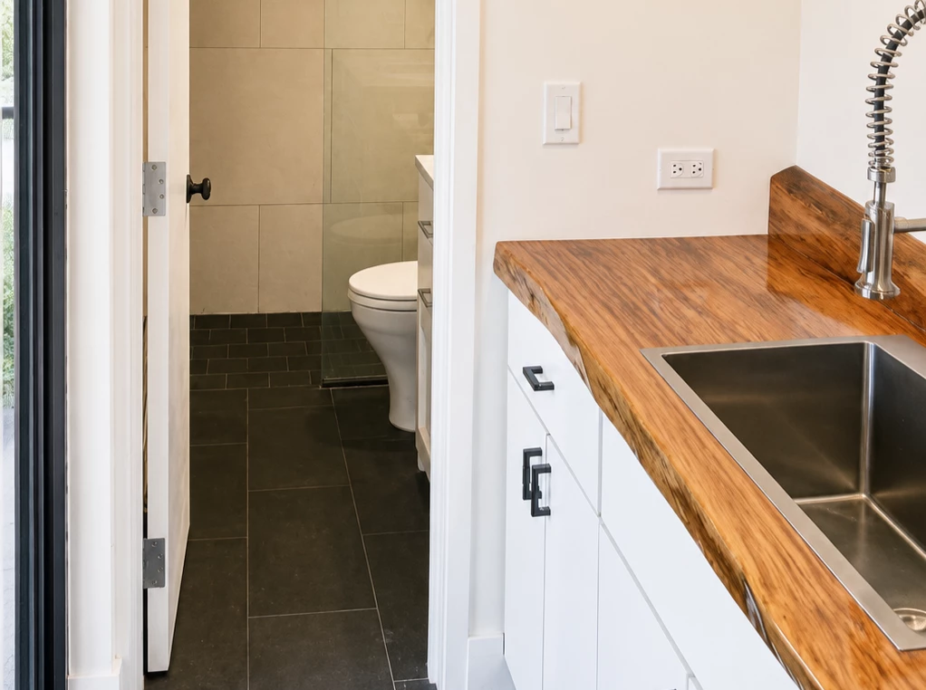A bathroom with a sink, toilet, and shower, featuring a wood countertop and white cabinets.