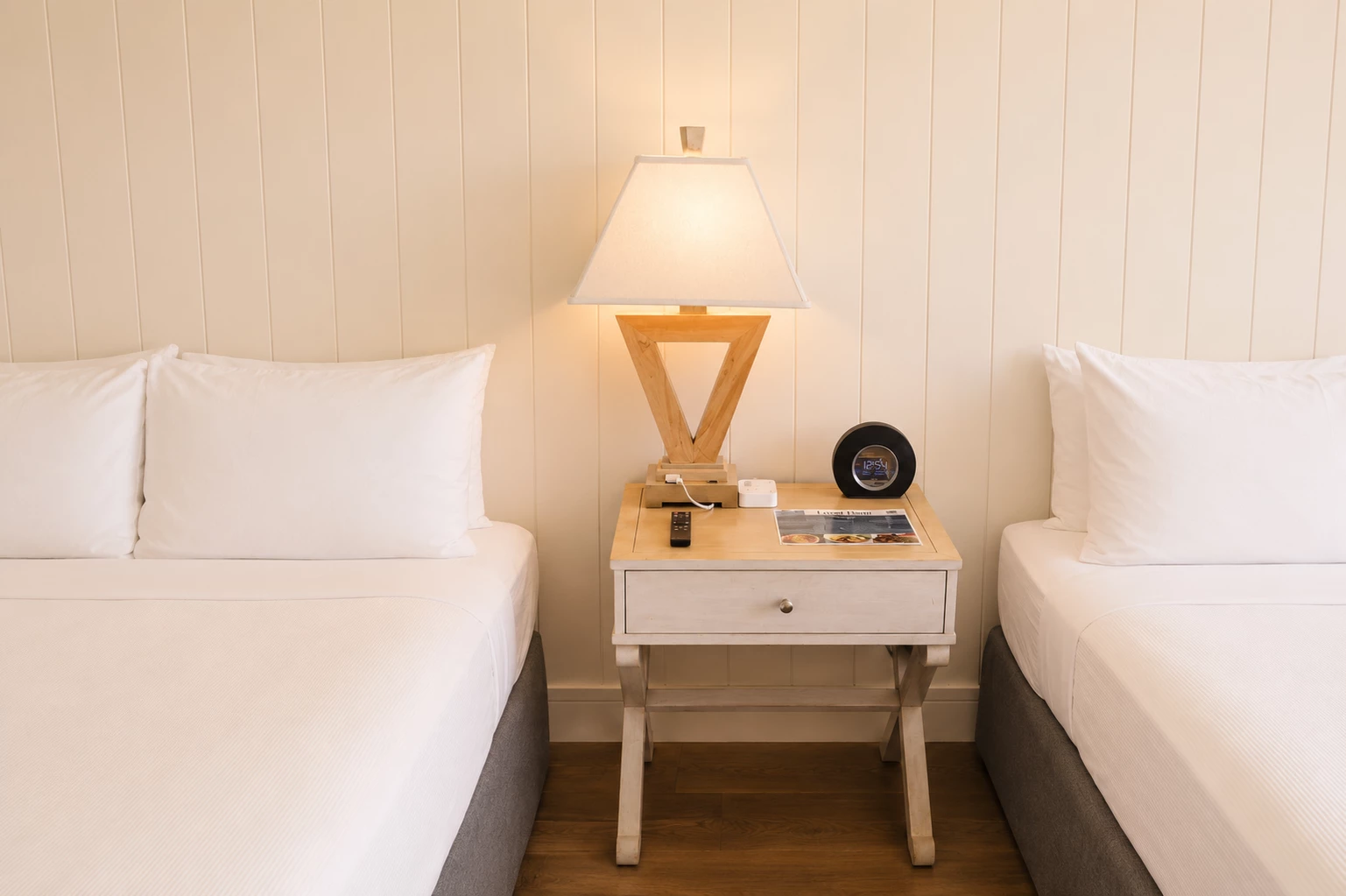A hotel room with two beds and a wooden nightstand between them.