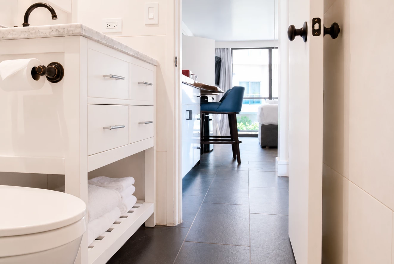 A modern bathroom with a white cabinet, marble countertop, and black fixtures, with a view of a room with a desk and window.
