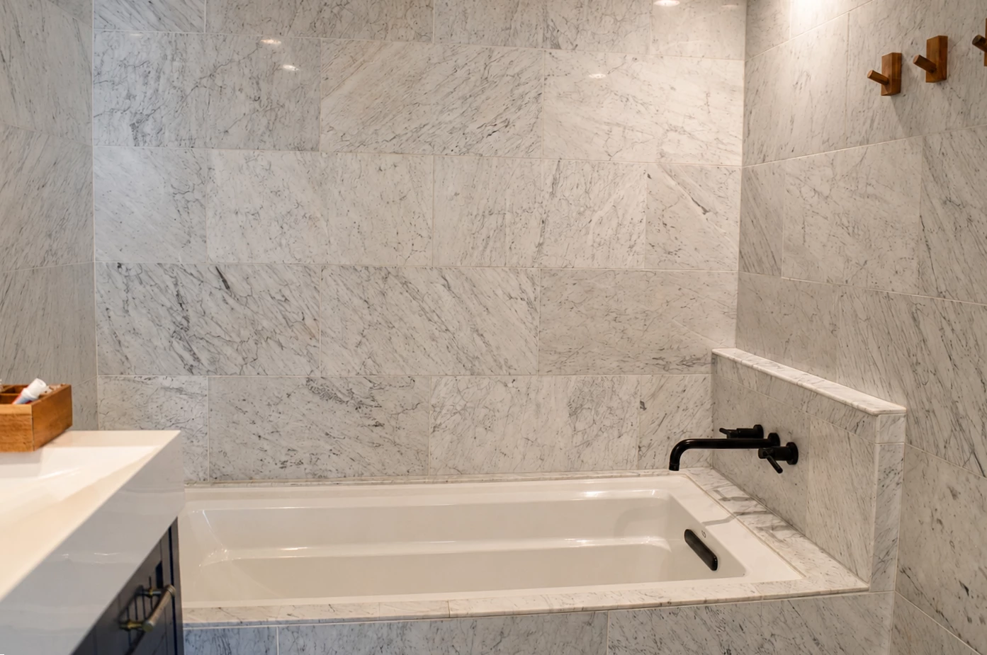 A bathroom with marble tiles, a white bathtub, and a black faucet