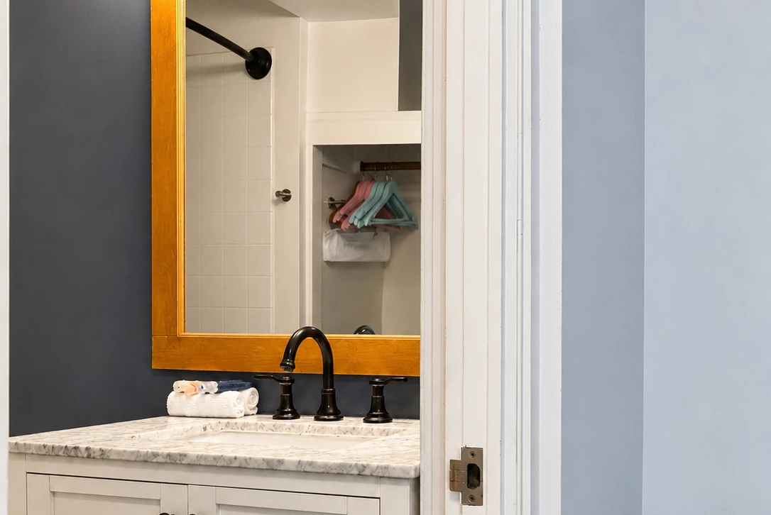 A bathroom sink area with a marble countertop, black faucet, and a mirror reflecting a closet with clothes hangers.