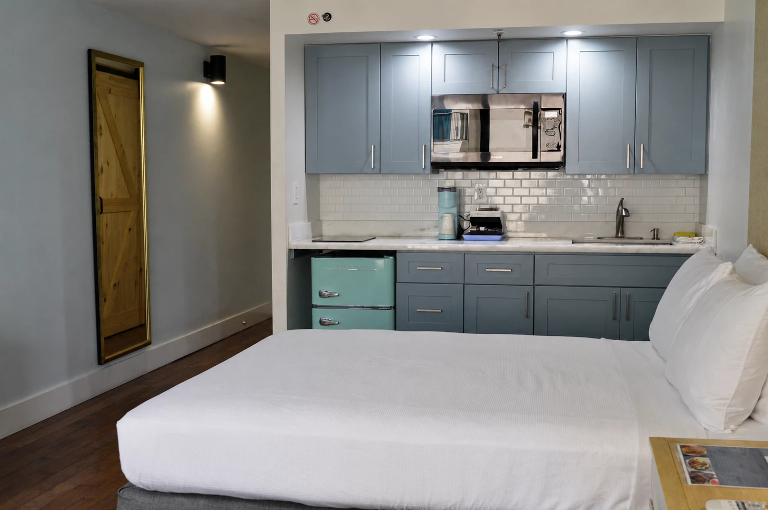 A hotel room with a kitchenette, bed, and white linens