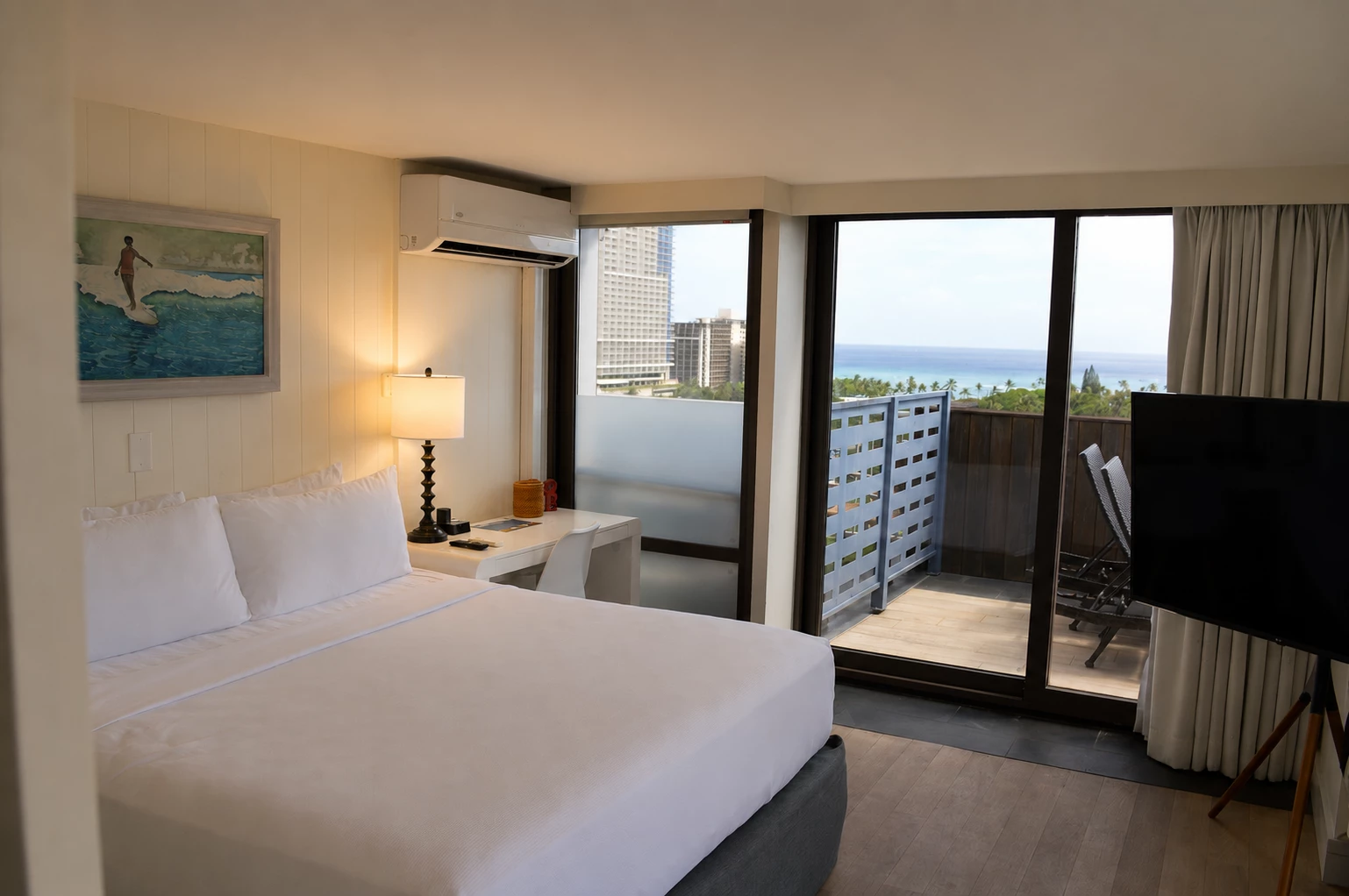 A hotel room with a bed, desk, lamp, TV, and balcony with a city view.