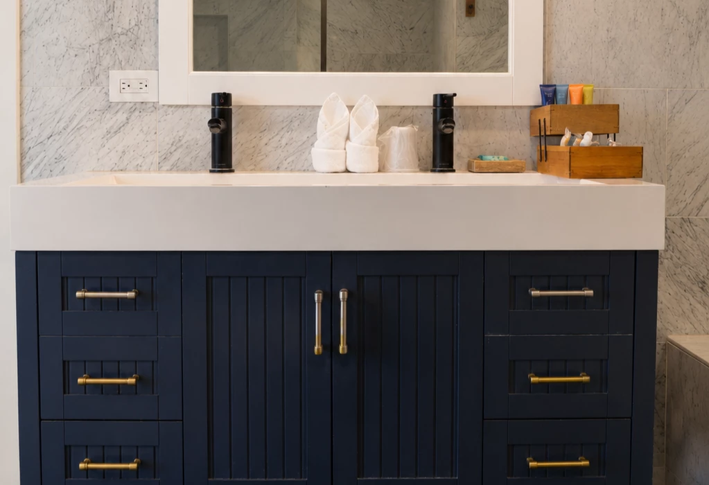 A close-up of a bathroom vanity with a white countertop, dark blue cabinets, and gold hardware.