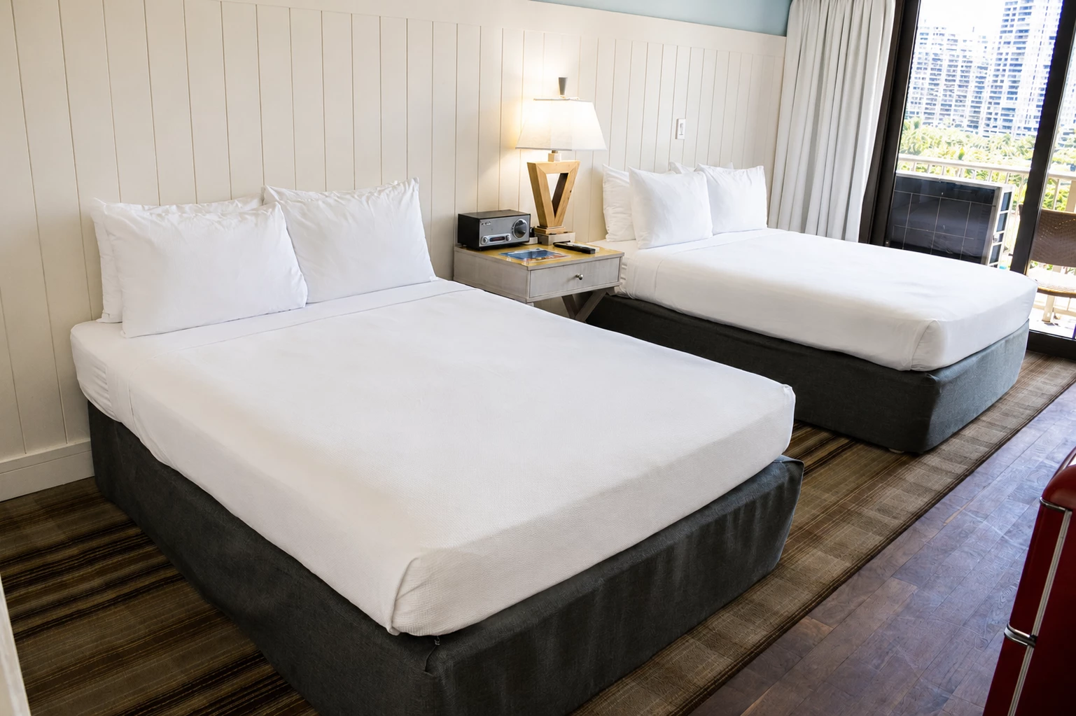 A hotel room with two twin beds, a nightstand, and a window with a city view.