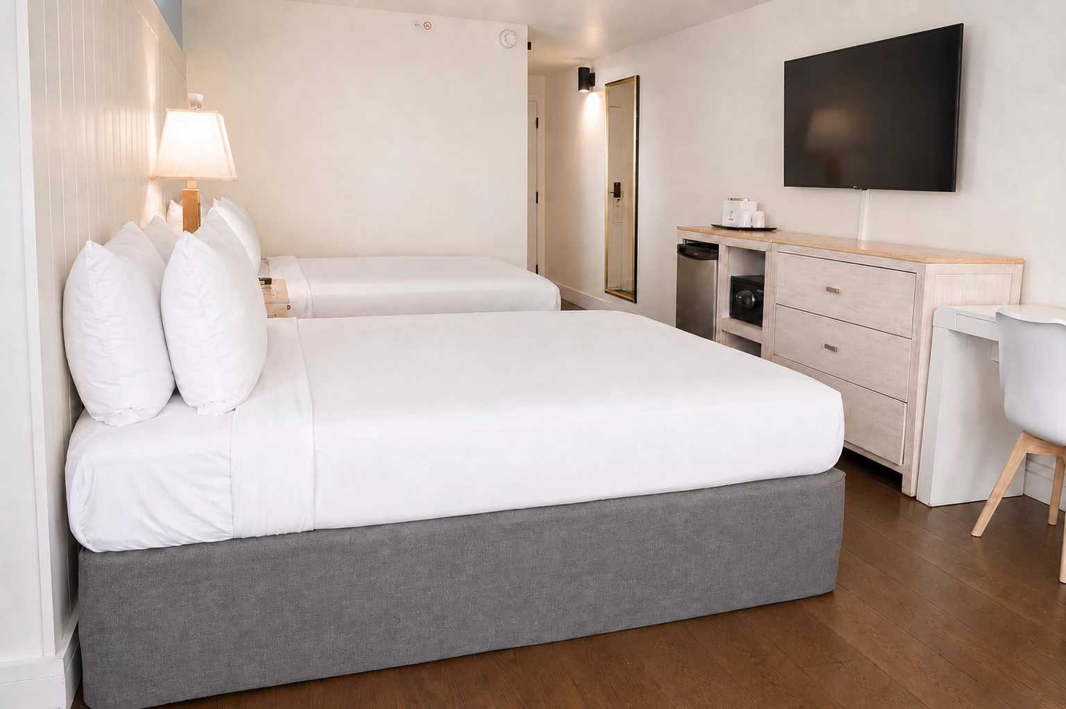 A hotel room with a double bed, a flat screen TV mounted on the wall, a desk, and a dresser.