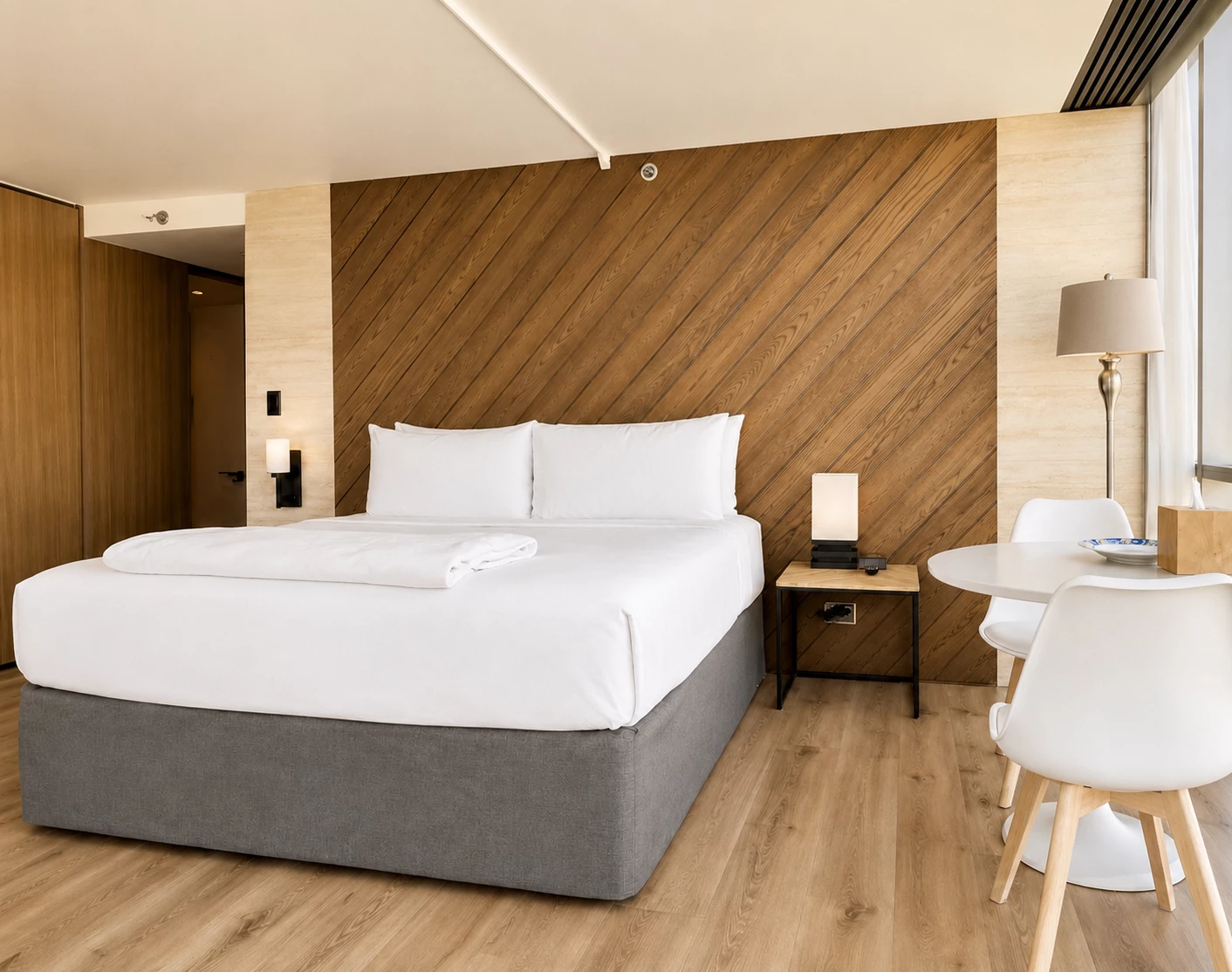 A hotel room with a bed, table, chairs, and lamp.