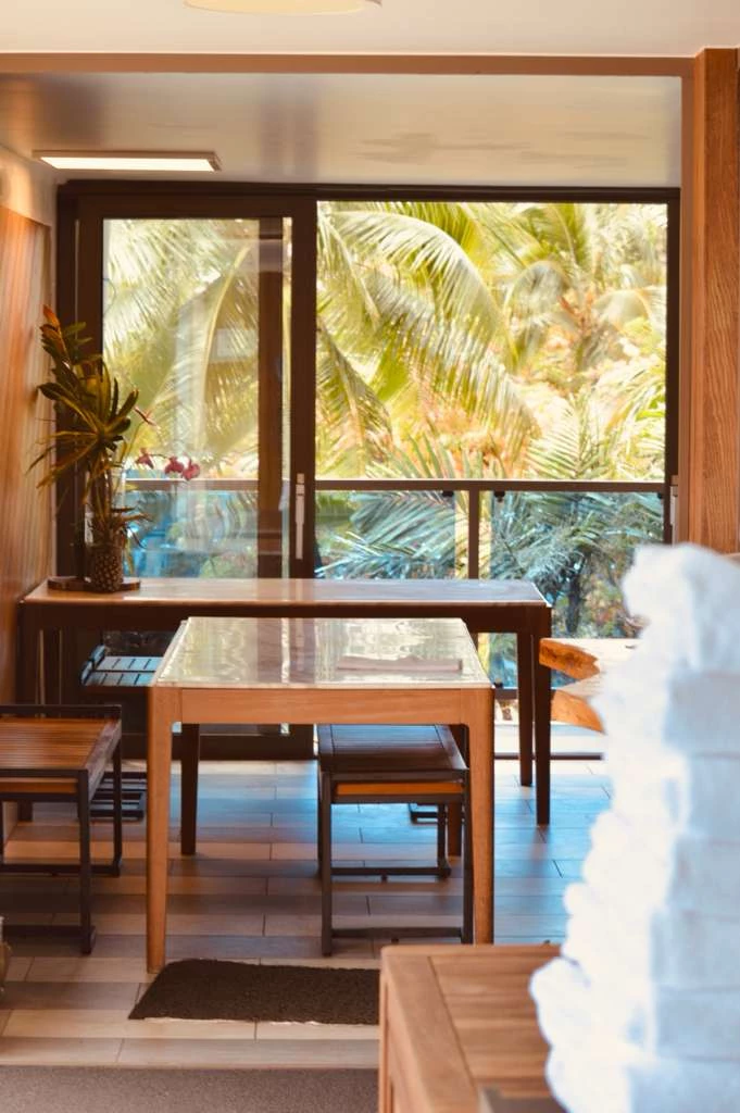 A dining area with a wooden table and chairs, and a large window showing palm trees outside.