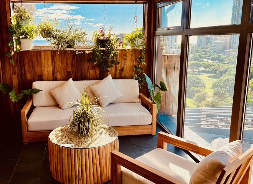 A cozy lounge area with a sofa, chair, and coffee table, surrounded by plants and offering a view of the city.