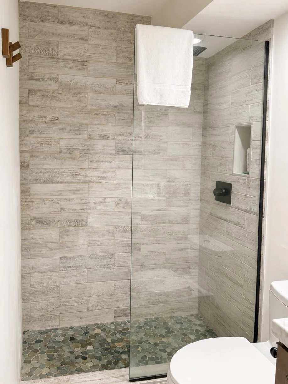 A modern bathroom shower with a glass door, tiled walls, and a pebble floor.