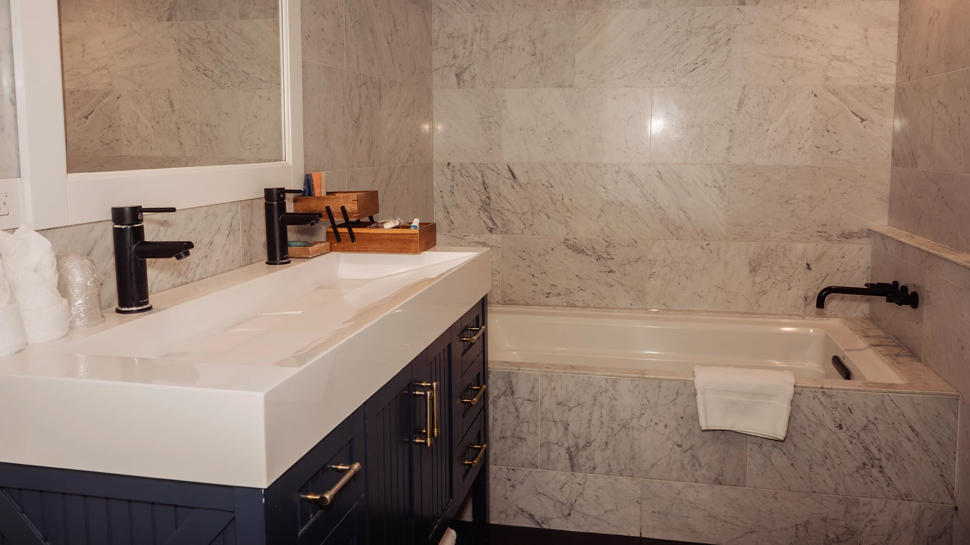 A bathroom with a white sink, black cabinet, and bathtub with marble tiles.