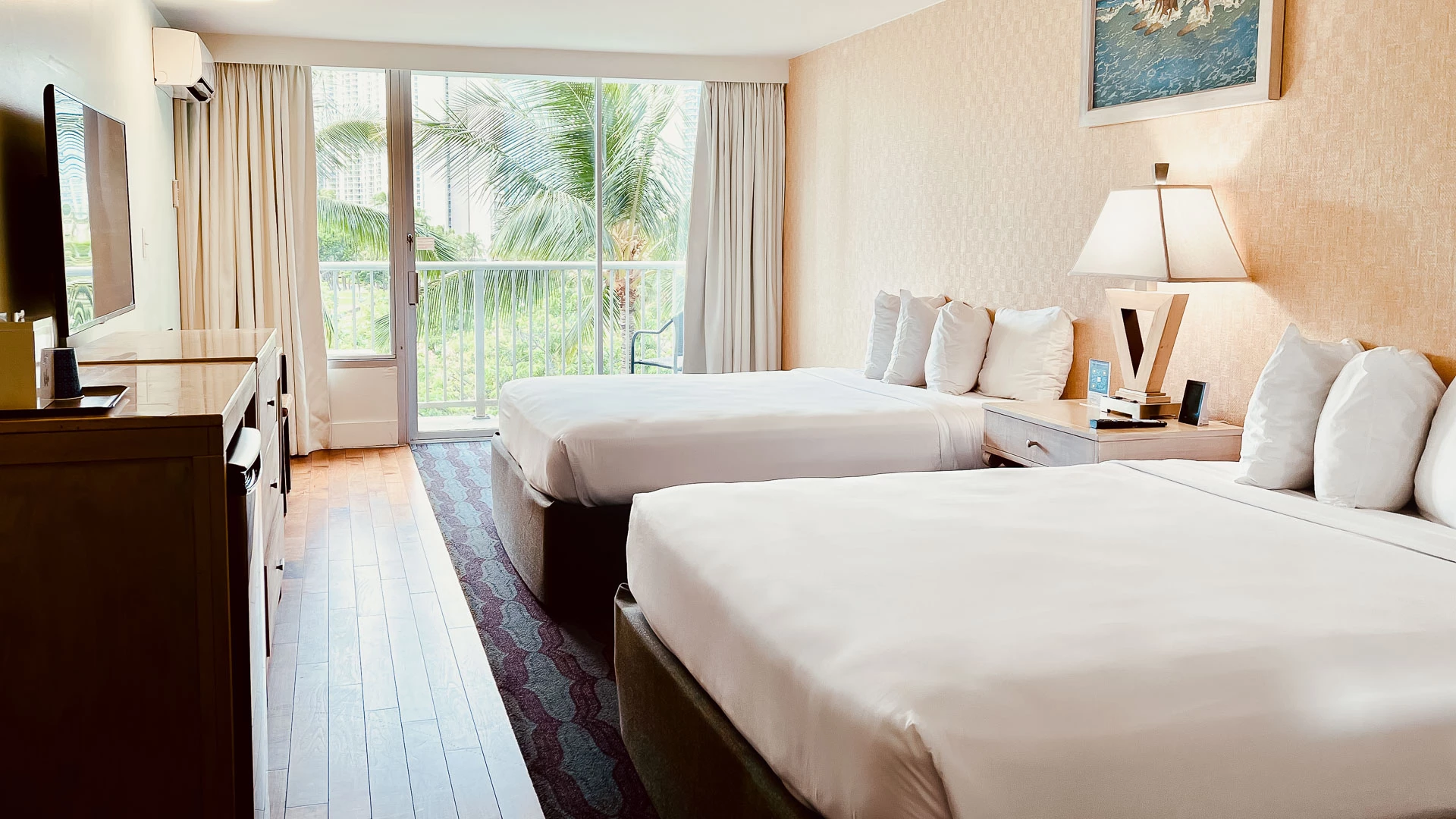 A hotel room with two twin beds, a balcony, and a view of palm trees.
