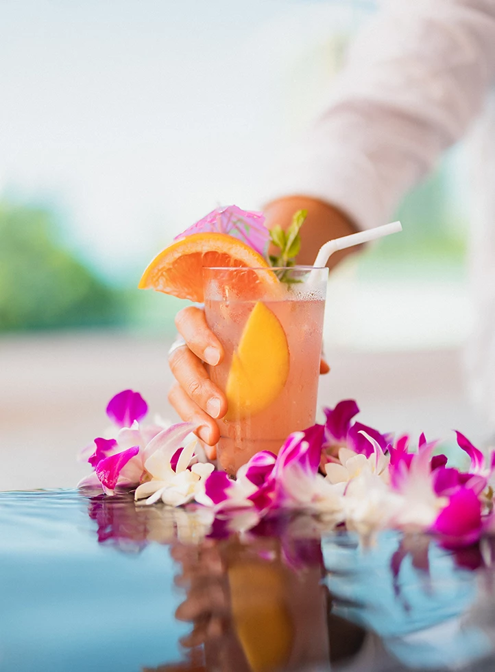 a hand holding a drink with flowers around it