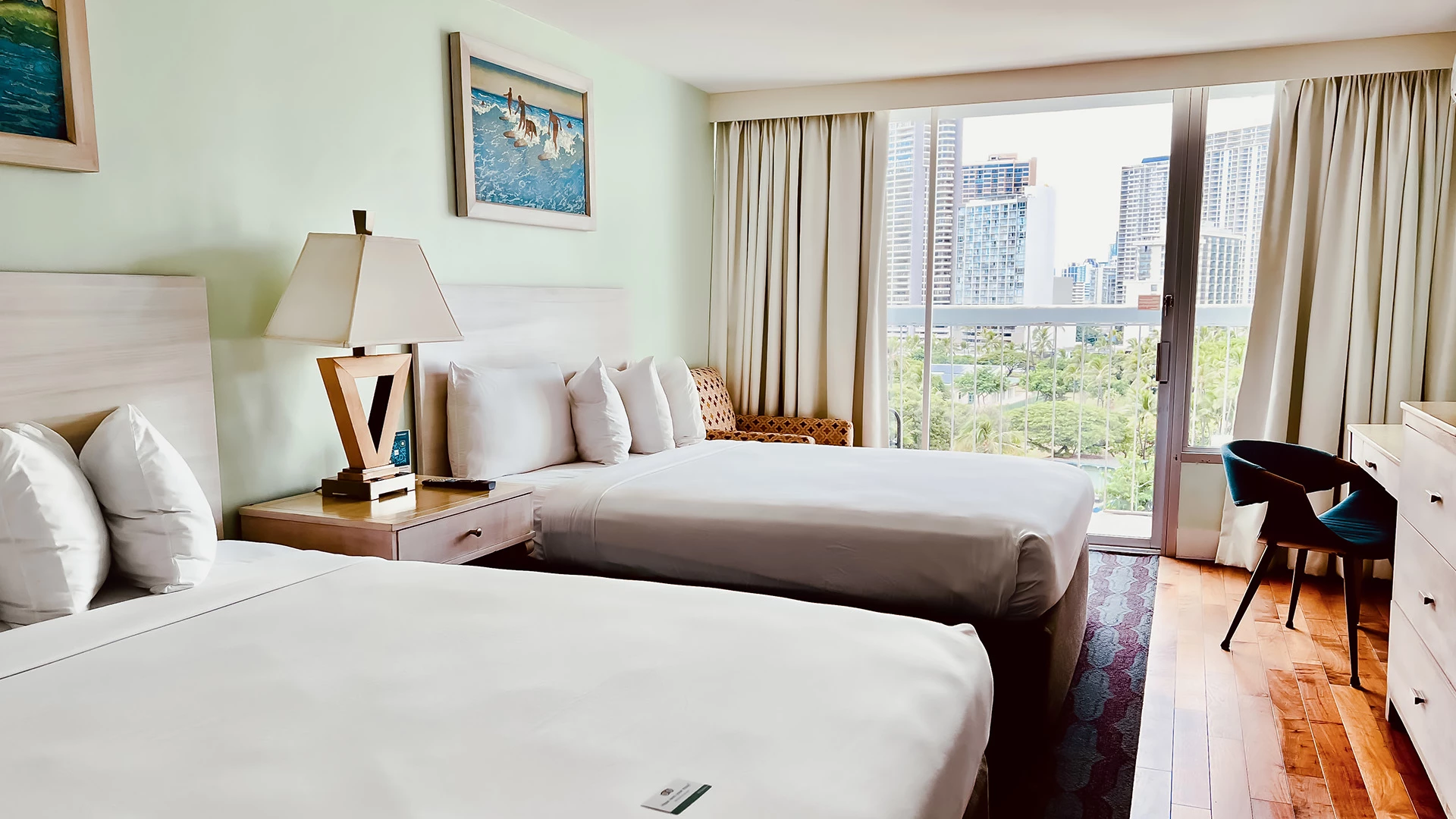 A hotel room with two beds, a window with a city view, and a desk.