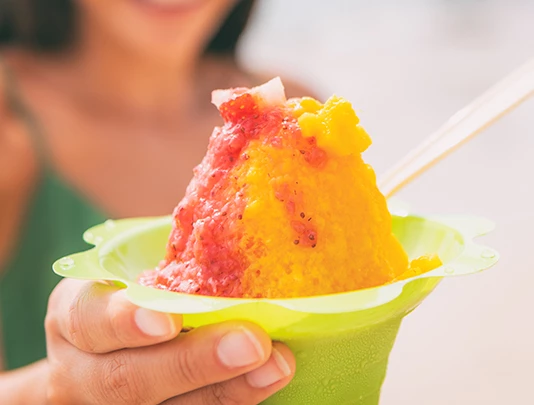 A hand holding a green cup with a colorful shave ice dessert