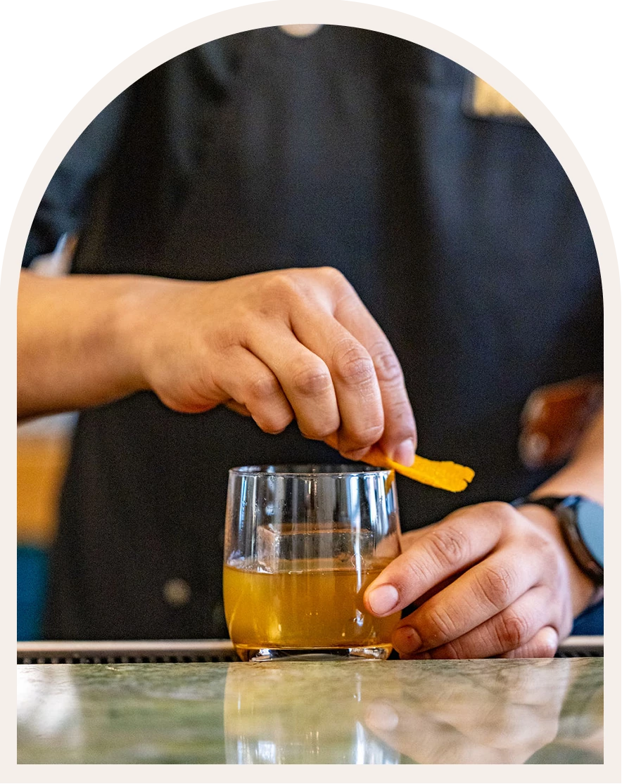 a person putting orange peel into a glass of liquid