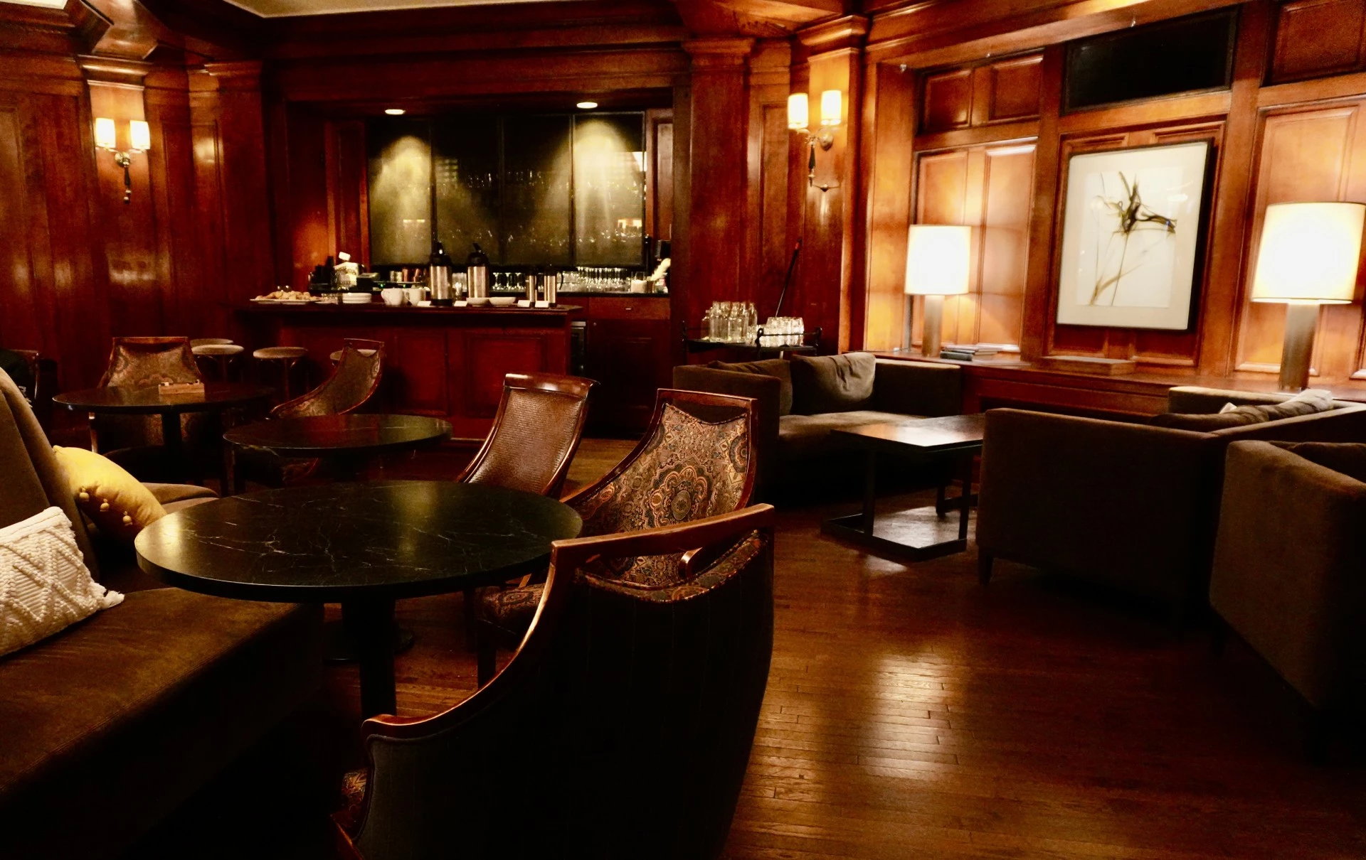 A dimly lit lounge with wood paneling, leather chairs, and sofas.