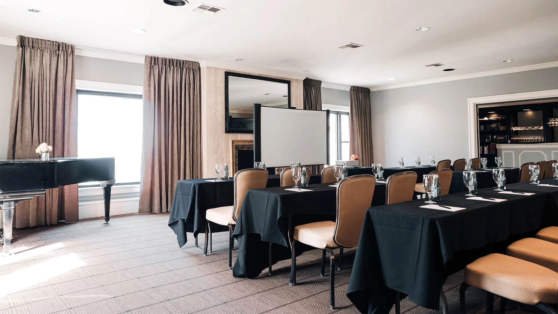 A meeting room with black tablecloths, brown chairs, a piano, and a projector screen.