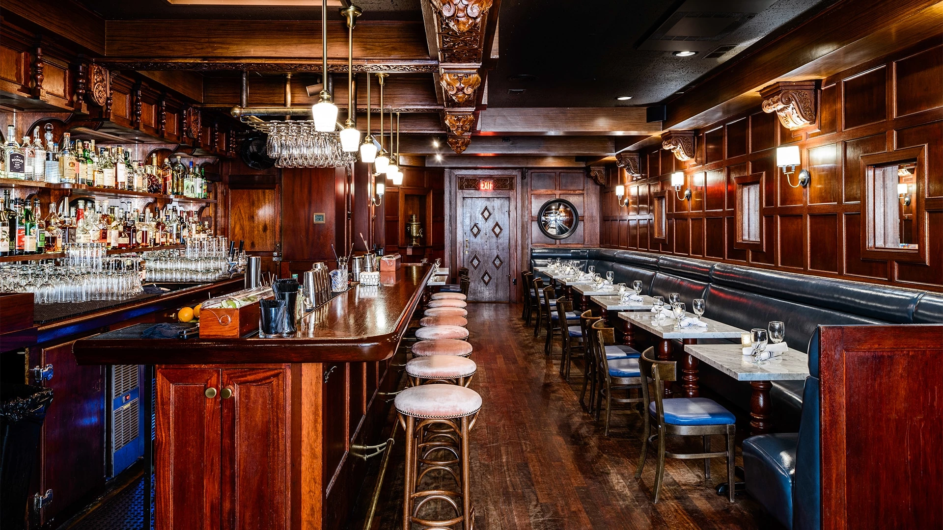 A dimly lit bar with a wooden counter, stools, booths, and tables.
