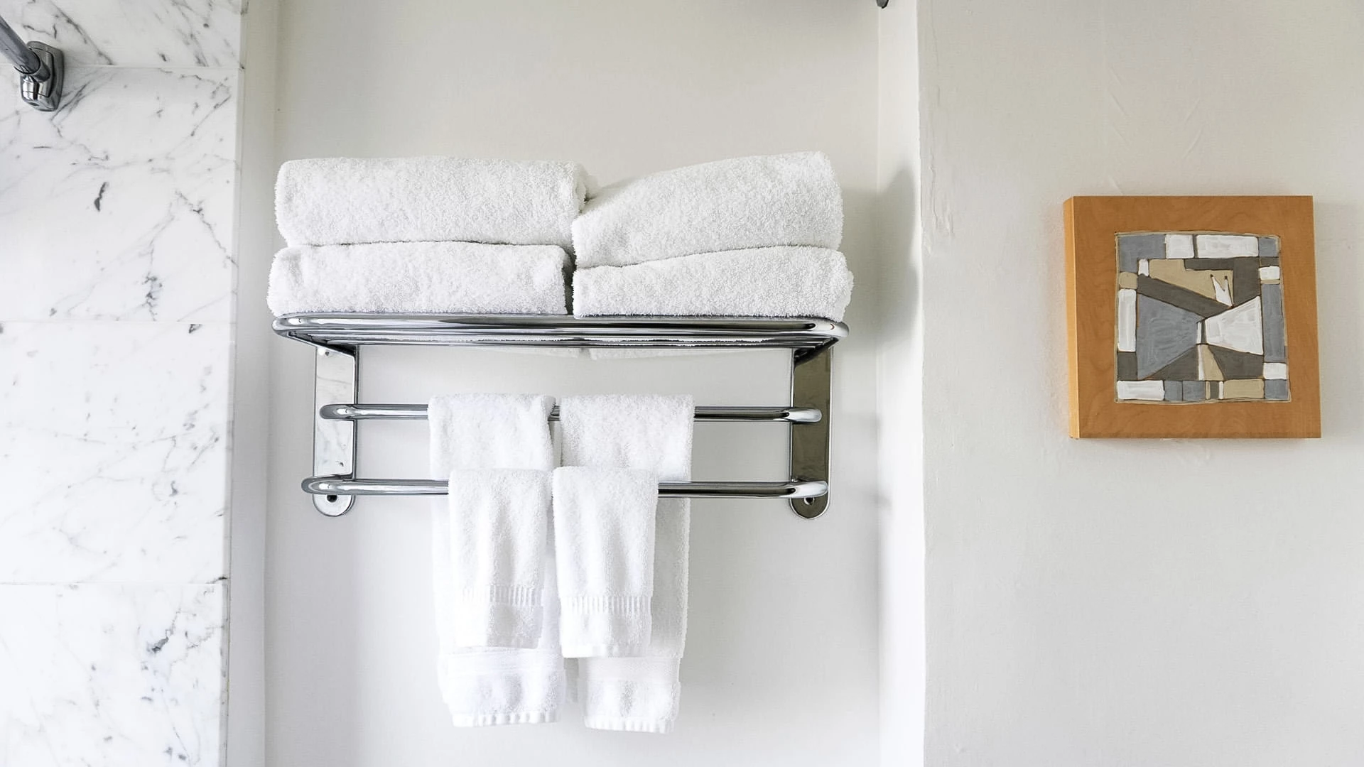 A bathroom with a marble wall, a towel rack with white towels, and a piece of artwork.