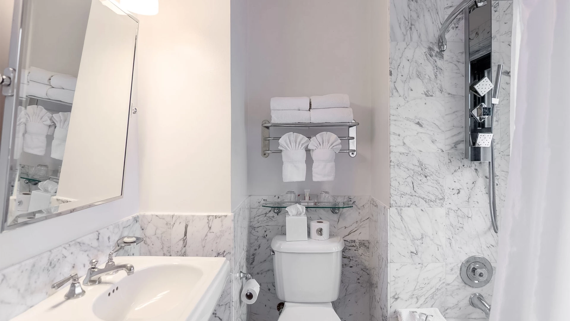 A standard bathroom with marble tiles, a white sink, toilet, and shower.