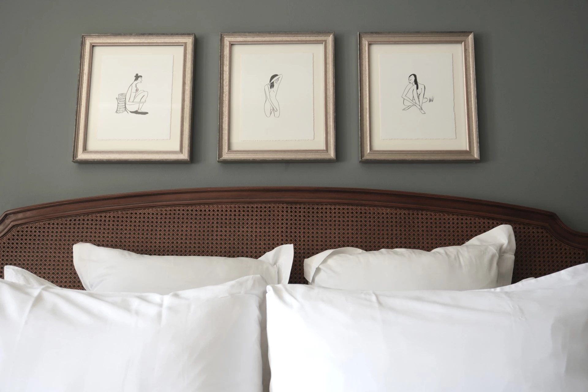 A close-up of a bed with white bedding and a wooden headboard with framed artwork above it.
