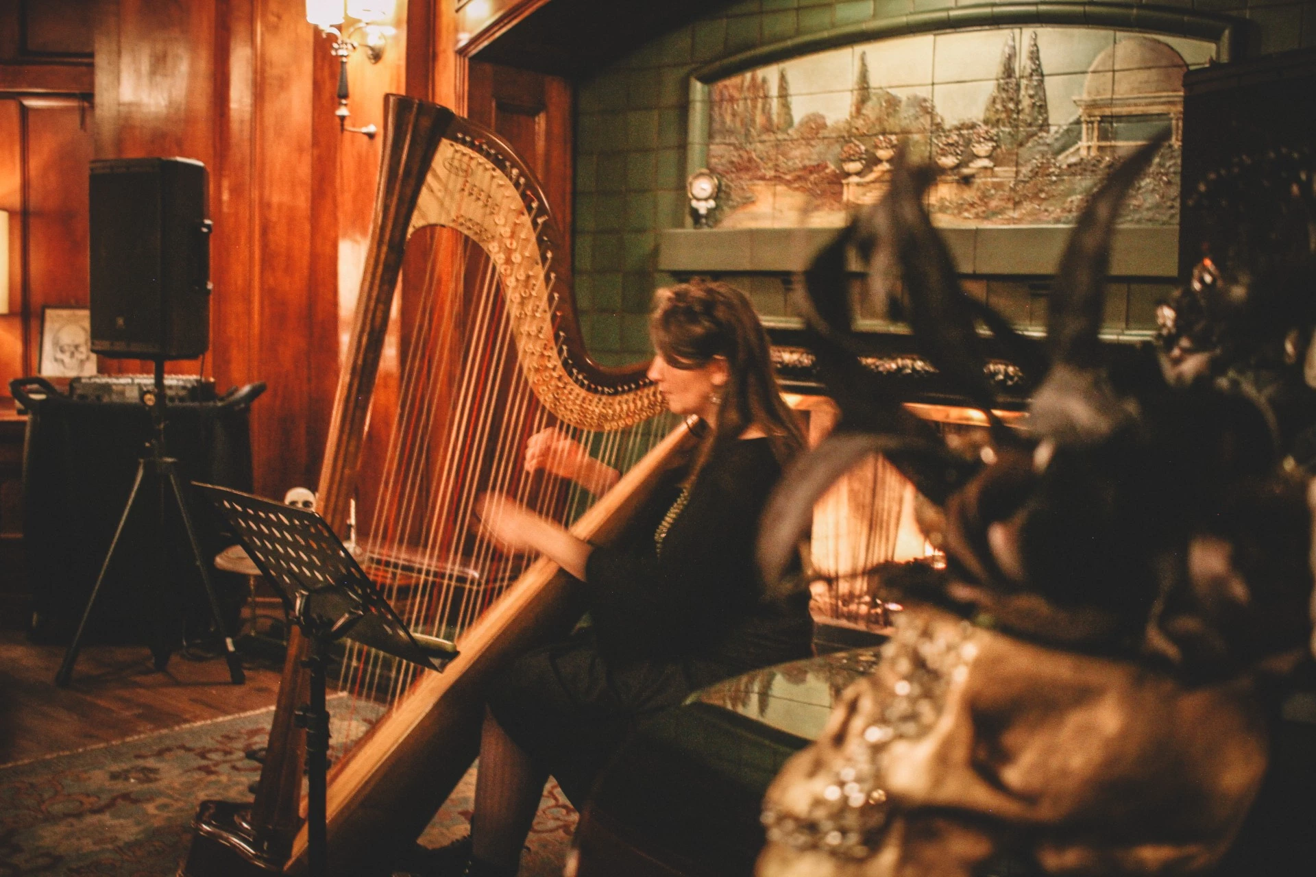 A woman plays the harp in a room with wood paneling and a fireplace.