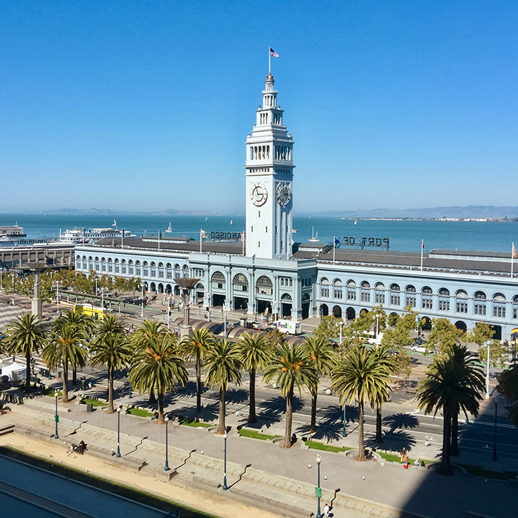a large white tower with a clock on it with San Francisco Ferry Building in the background