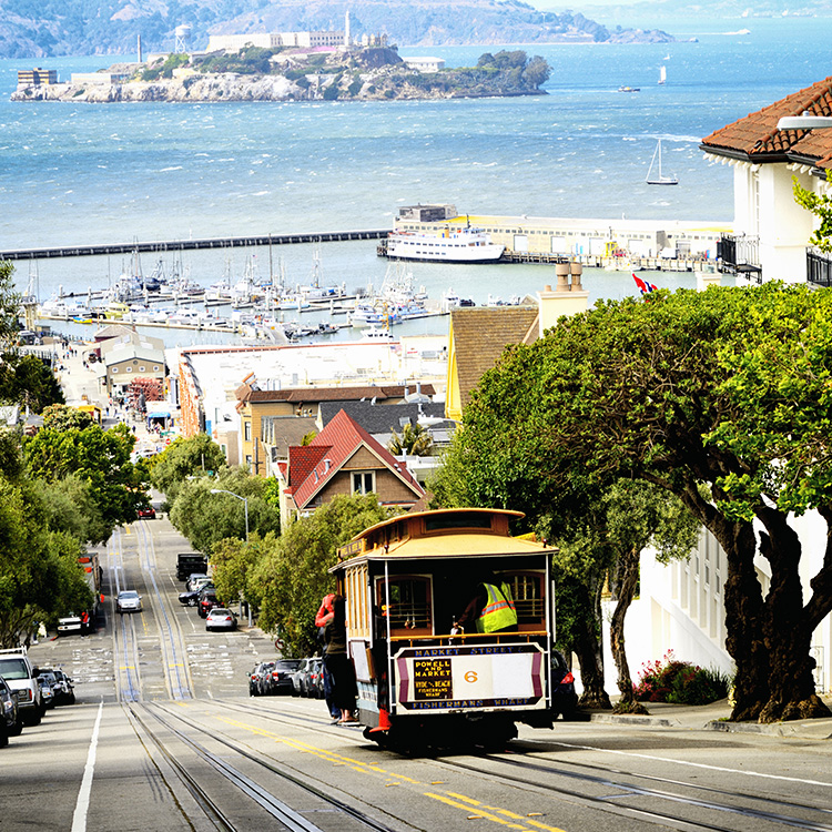 a trolley on a street with a city and water in the background