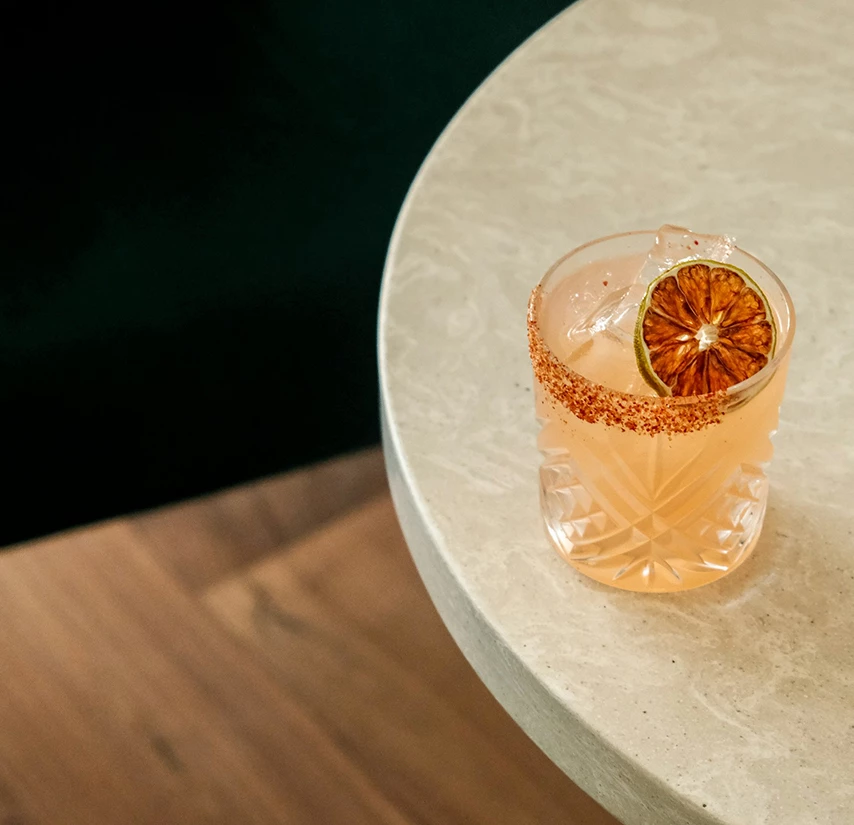 a glass of pink liquid with a slice of orange and a slice of lime on a white table