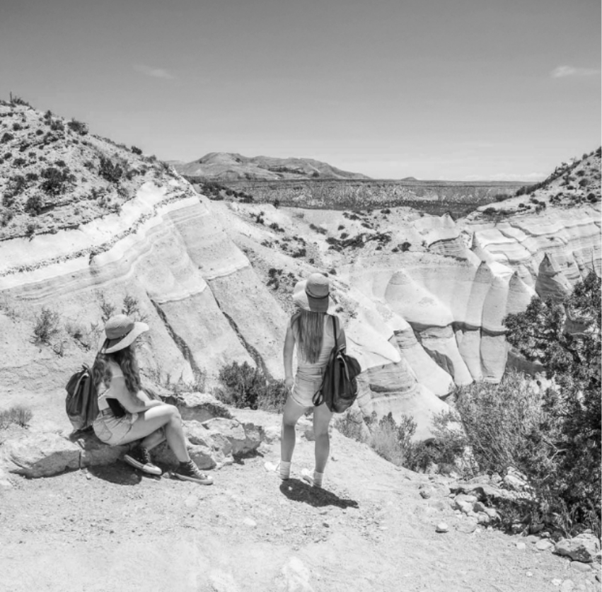 two women sitting on a hill looking at a canyon